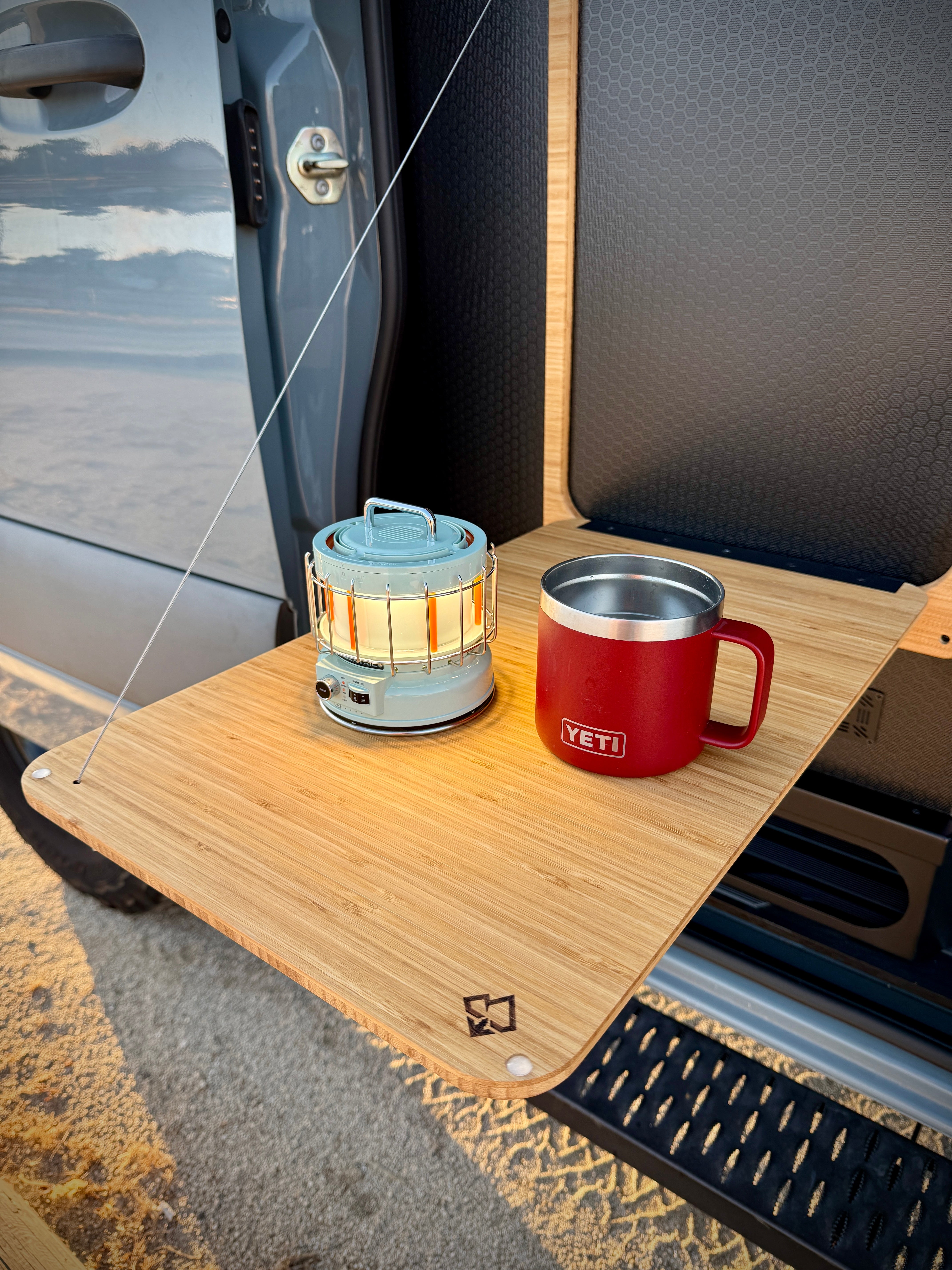 Bamboo folding table attached to a vehicle door with a lantern and red YETI mug on top.